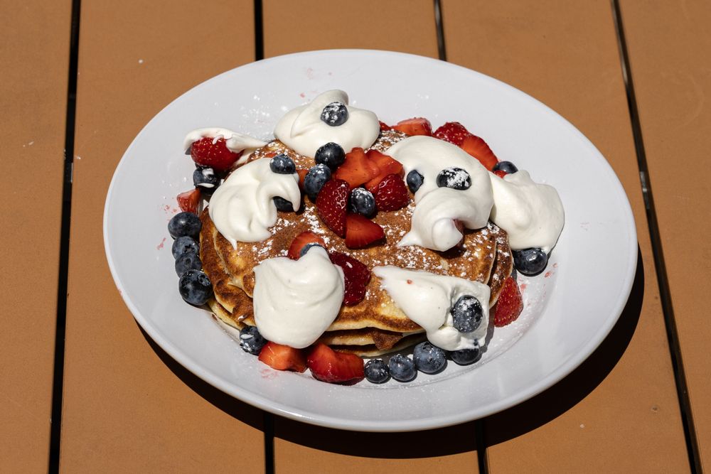 Pancake stack topped with berries, powdered sugar, and white cream